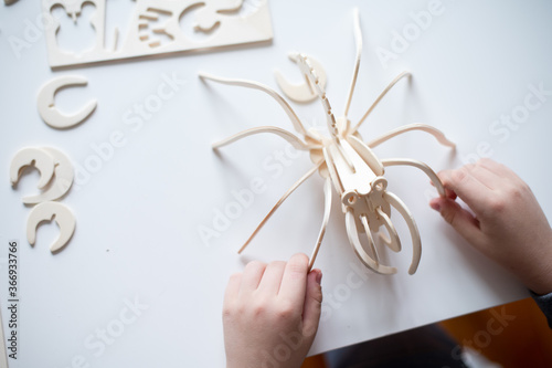 hands of a child and a wooden spider on the table  which the boy build