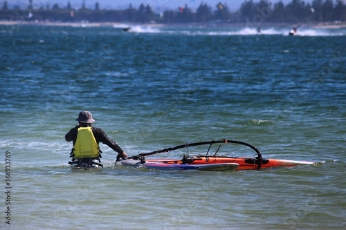 Man dressed in sun protective clothing taking his windsurfer out to deeper water. Kyeemagh beach, Sydney photo