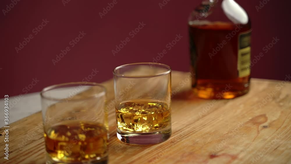 Old tasty whisky with ice cubes in crystal glasses on wooden board in local bar. Bottle of scotch whiskey for relaxation after stress or work. Ancient alcohol drink Old tasty whisky with ice cubes in crystal glasses on wooden board in local bar. Bottle of scotch whiskey for relaxation after stress or work. Ancient alcohol drink