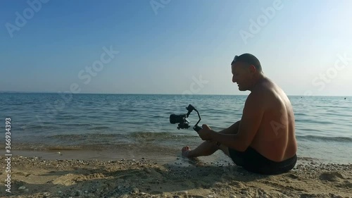 Senior videographer recording videos with gimbal of the beach and calm sea