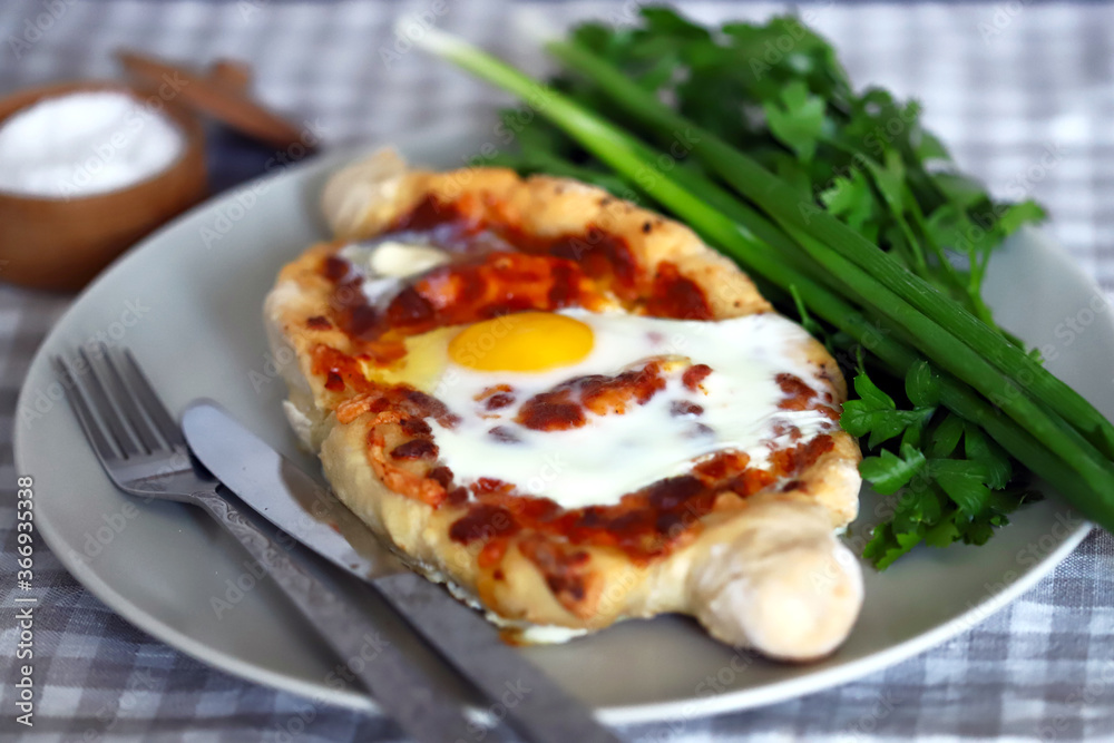 Selective focus. Macro. Khachapuri with egg and herbs on a plate.