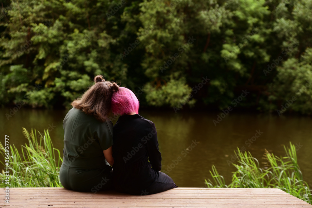 two friends sit on the Bank of a quiet river in summer
