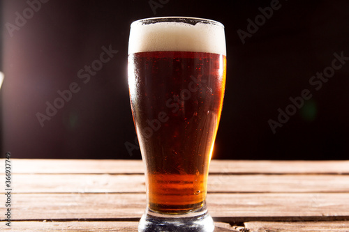 Cold tasty beer on hot summer day. Glass of beer on wooden table on black background