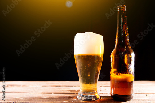 Cold tasty beer on hot summer day. Bottle and glass of beer on a wooden table against black background and copy space