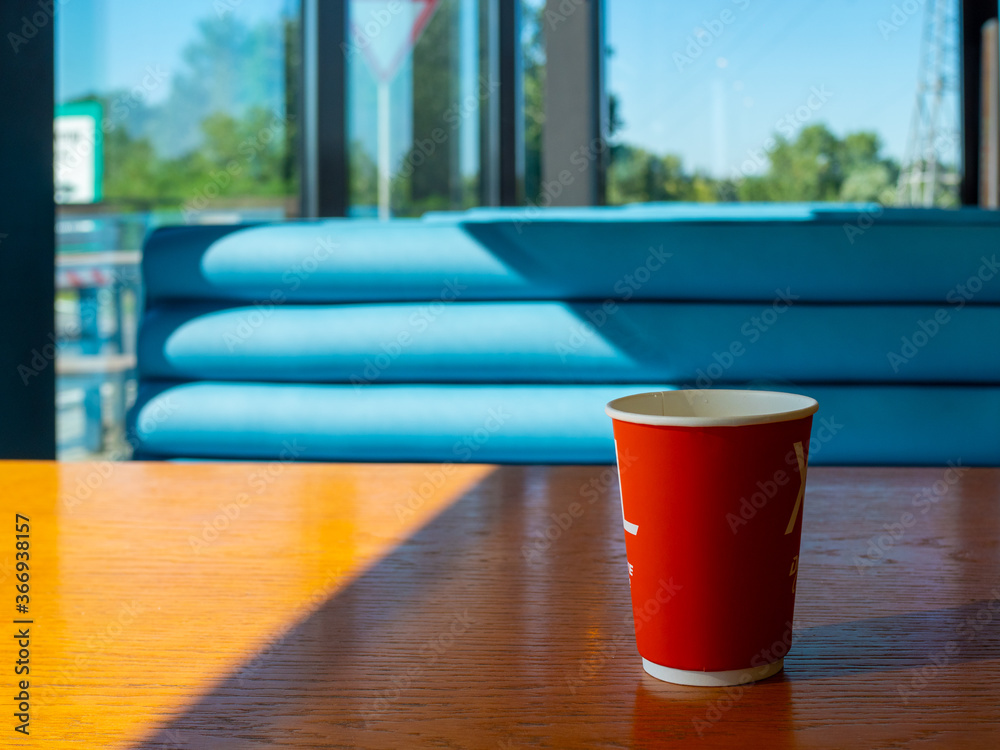 Red cup of coffee stands on a wooden table in a gas station cafe. Morning coffee