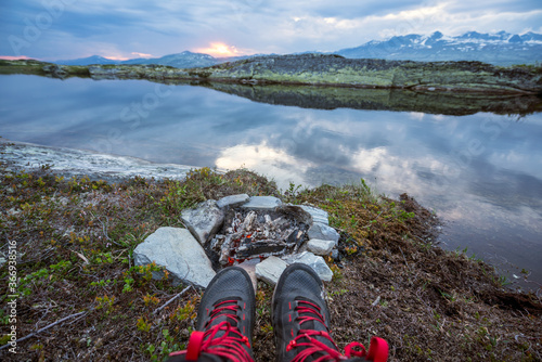 Hiking boots infront of burned out bonfire in camp. With lake and mountain view.