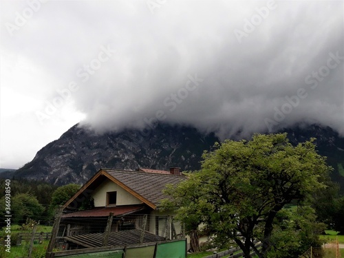 Old damaged, empty house in front of a mountain and a large white cloud 