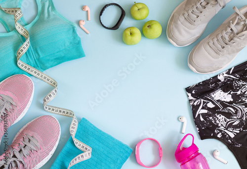Top view of sport accessories with copy space. Running shoes, bras, bottle, earphones, towel, measuring tape on blue table
