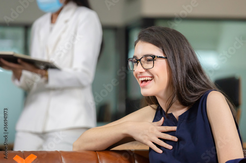 Cheerful young woman in eyeglasses sitting on sofa in modern office, new normal concept