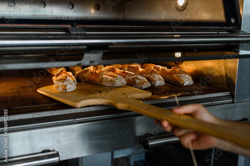 Fotografia Close up of baker is taking off from oven the french baguette bread with wood pe