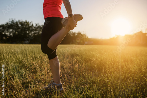 Young beautiful woman is making sport, she is doing the legs exercises on a grass in the midst of nature on sunset and preparing for running. © Med Photo Studio