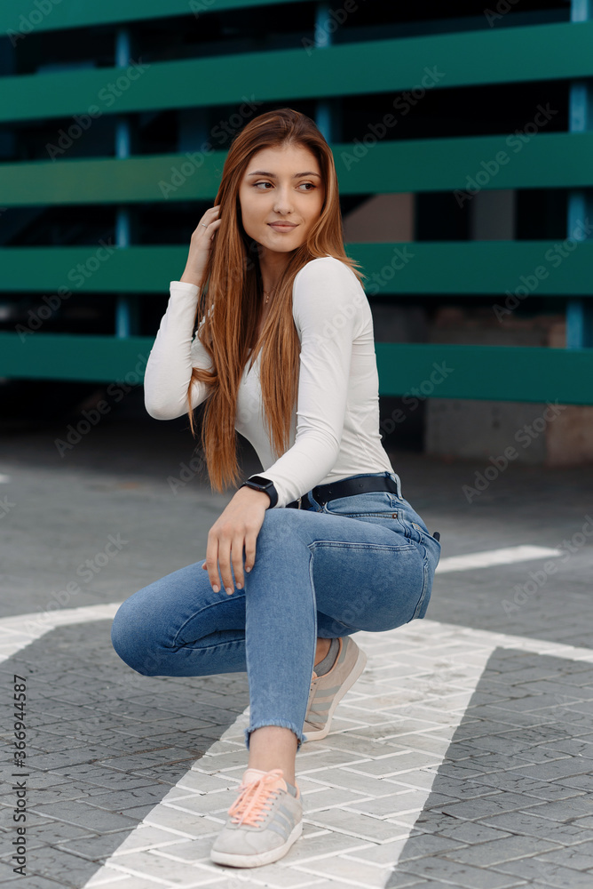 Stylish girl posing at the street, dressed in blue jeans and a white T-shirt