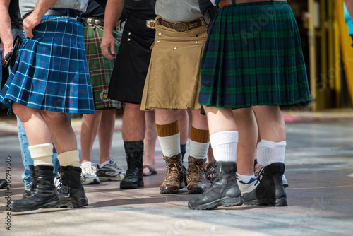 St. John's, NL/Canada - A group of men wearing kilts on a street. Some have boots on and others sneakers. The kilts are both green,blue,tan and have a pattern on them.The view is from the waist down.