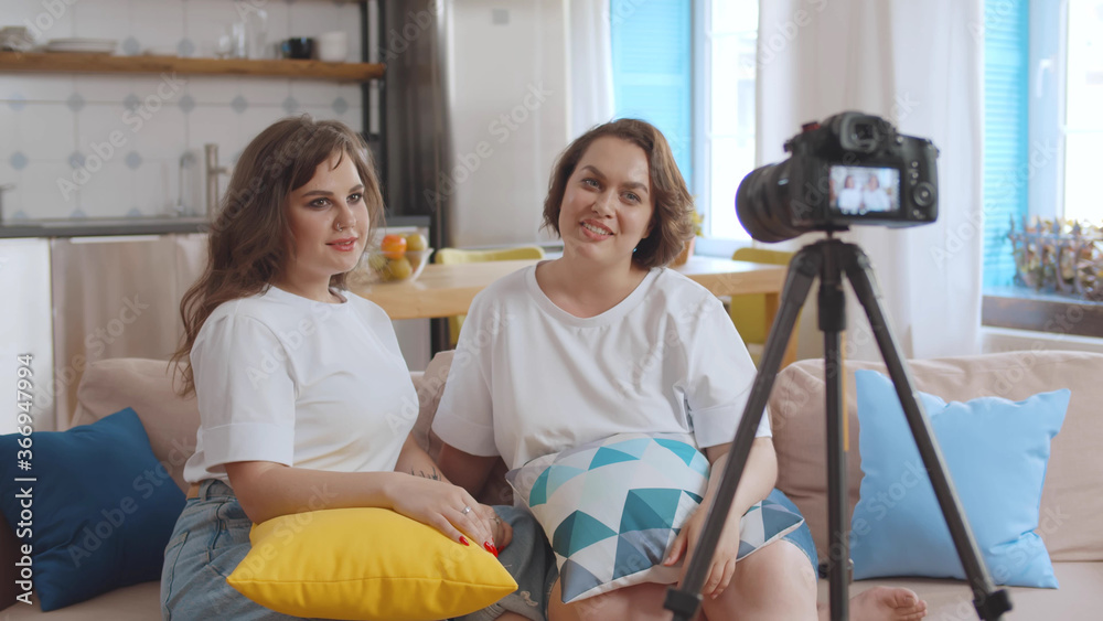 Obraz premium Two beautiful plus size girlfriends shooting video for internet blog sitting at home
