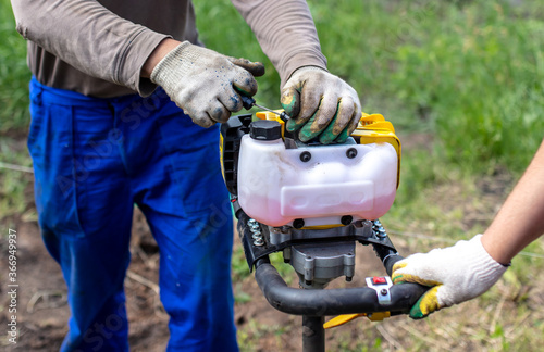 A worker is drilling soil for a gate on a fence.