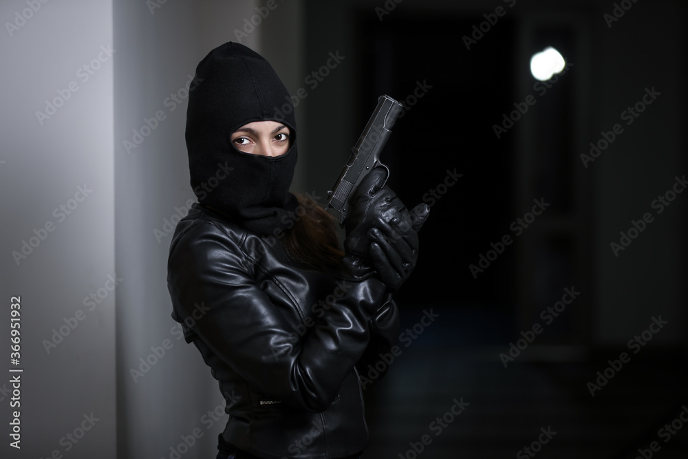 Thief broke into the apartment. House robbery by woman in a black jacket and black mask holding black gun. Burglar in a mask. Thief in a mask trying to break into other people's house