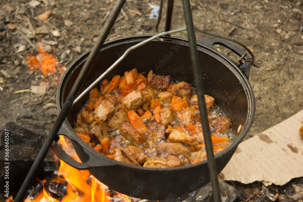 Cooking camping outdoor meal in an open fire in a travel pot with blaze. Dinner during travel. Cooking camping outdoor meal in an open fire in a travel pot with blaze. Dinner during travel.