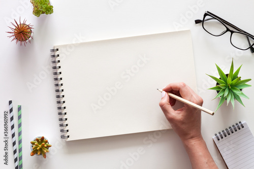 A white desk with an open sketchbook and a woman's hand. Drawing. View from above. Creative desk. Mockup.