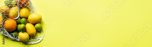 top view of ripe whole citrus fruits in string bag on yellow background, panoramic crop