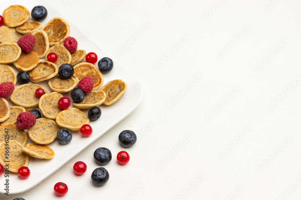 Mini pancakes and berries in plate. Red currants, blueberries on white background Mini pancakes and berries in plate. Red currants, blueberries on white background