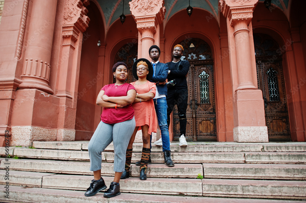 Four african friends posed outdoors against old architecture. Two black girls with guys.