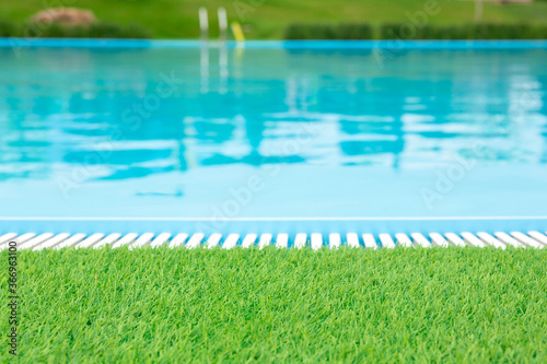 Natural background. Green lawn grass on the background of a pool with clear blue water. For montage of your product
