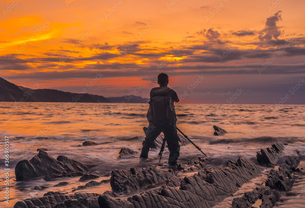 A photographer in the orange sunset on the beach of Sakoneta and his beautiful Flysch in the town of Deba, At the western end of the Basque Coast Geopark, Guipúzcoa. Basque Country