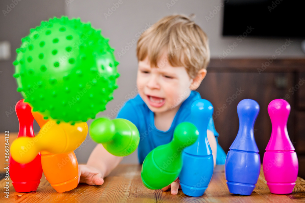 Obraz premium Children a boy throws ball into a home bowling alley and smashes the bowling pins. Selective focus. concept of active play in the home room, quarantine, self-isolation, achieving goal.