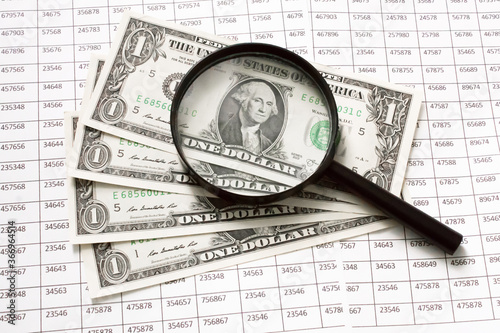 Looking through magnifying glass to the dollars banknotes and financial report.magnifying glass and money in the foreground, digital background. Finance