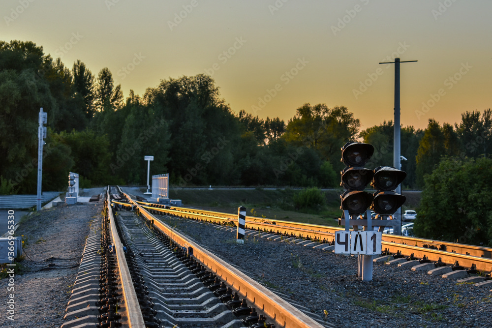 Railway traffic light and rails on the background of the setting sun. Railroad tracks at sunset. Railway traffic light and rails on the background of the setting sun. Railroad tracks at sunset.