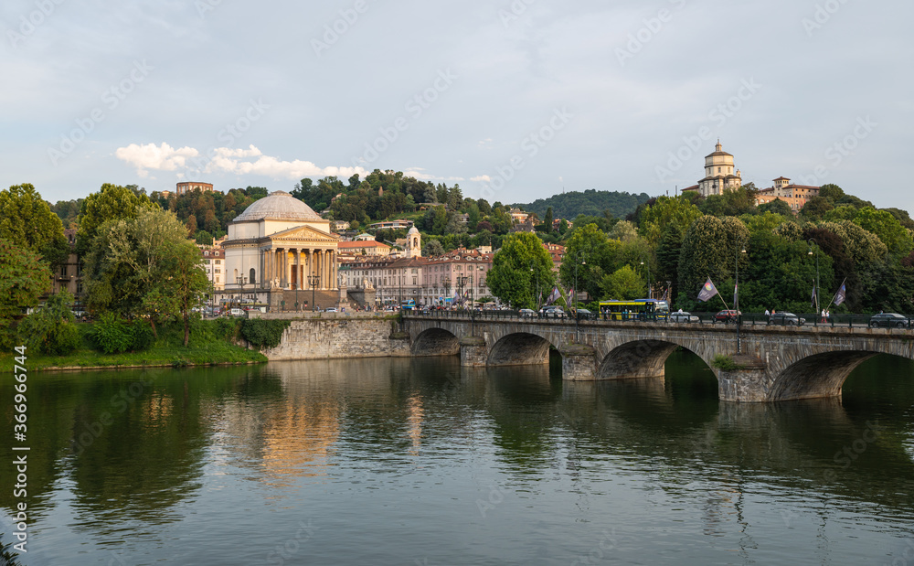 Turin, Piedmont, Italy. July 2020. Wonderful evening view of the Gran Madre church overlooking the Po river. The waterfall downstream of the dam is highlighted. On the bridge people and cars.
