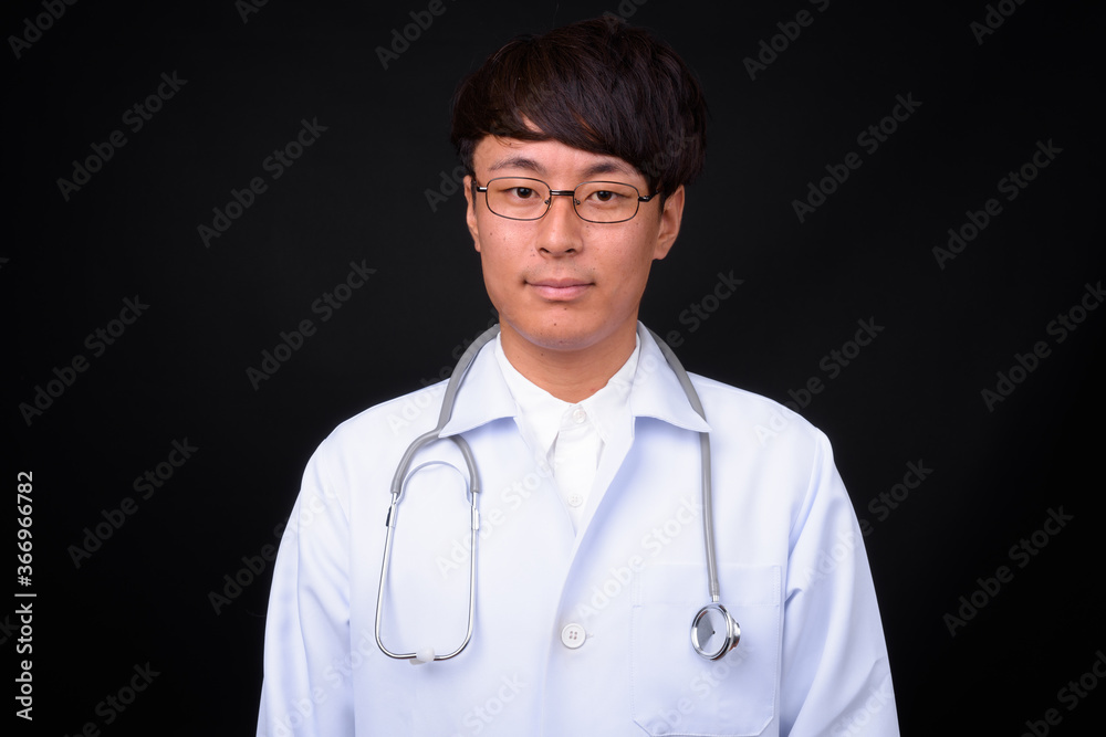 Young handsome Asian man doctor against black background Young handsome Asian man doctor against black background