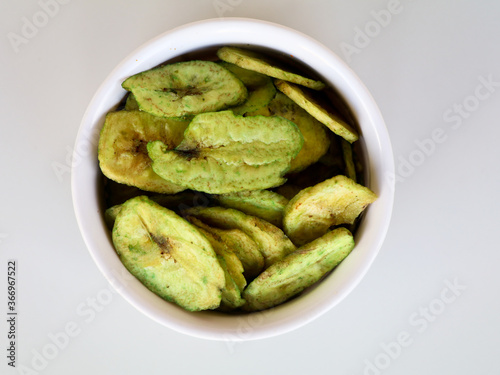 Green color banana chips with hot green chili flavor in a white bowl against white background