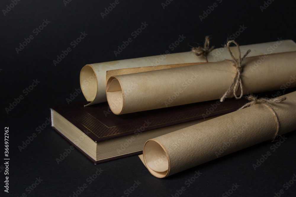 Old scrolls lie on the book. Education concept. Ancient knowledge. Photo on black background