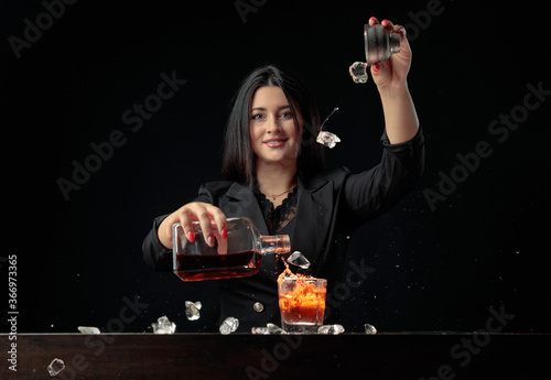 Εκτύπωση καμβά Attractive bartender girl pours an alcoholic drink into a glass and throws pieces of ice