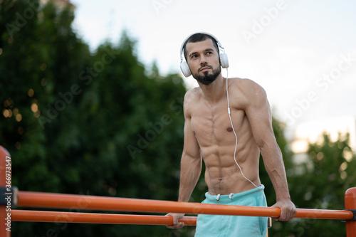 A man with headphones doing push UPS on the bars on the street