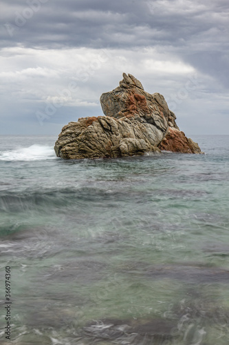 una roca rodeada de agua que parece un barco navegando con un mar verde