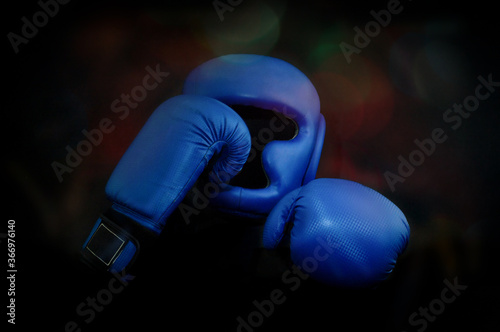 Two blue Boxing gloves and a protective helmet on a black background with rainbow highlights. © АртГЛОБУС