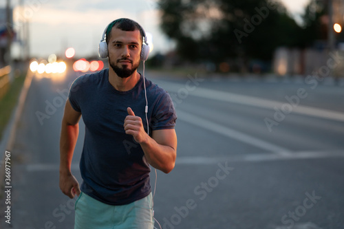 An athlete jogs through the city at night, a man runs in the evening on the road