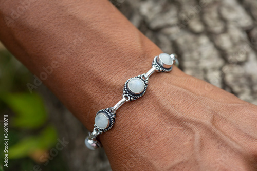 Bild auf Leinwand Outdoor closeup of a hand wrist wearing silver metal bracelet with moon stone ge