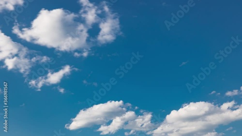 White clouds mooving on a blue sky over green field with grass and trees timelapse photo