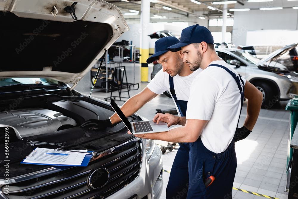 Auto mechanics looking at laptop screen near open hood of car at service station Auto mechanics looking at laptop screen near open hood of car at service station