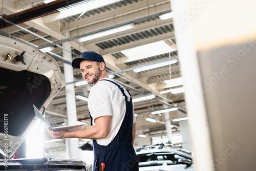 Happy auto mechanic holding laptop at service station