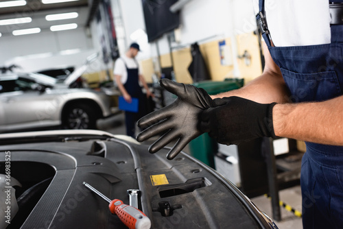 cropped view of mechanic in overalls wearing latex gloves near car in workshop