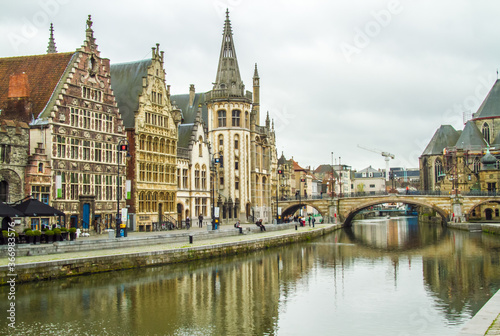 Ghent, Belgium; Public buildings and a church line a canal in Ghent. A stone bridge crosses the canal.
