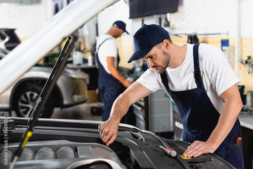 selective focus of mechanic in cap repairing car near coworker in workshop