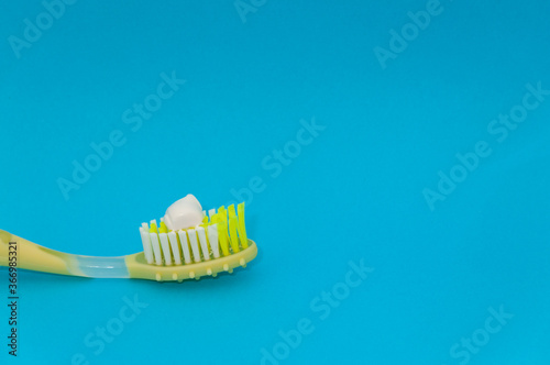 yellow toothbrush with the recommended size of toothpaste equivalent to a pea on blue background
