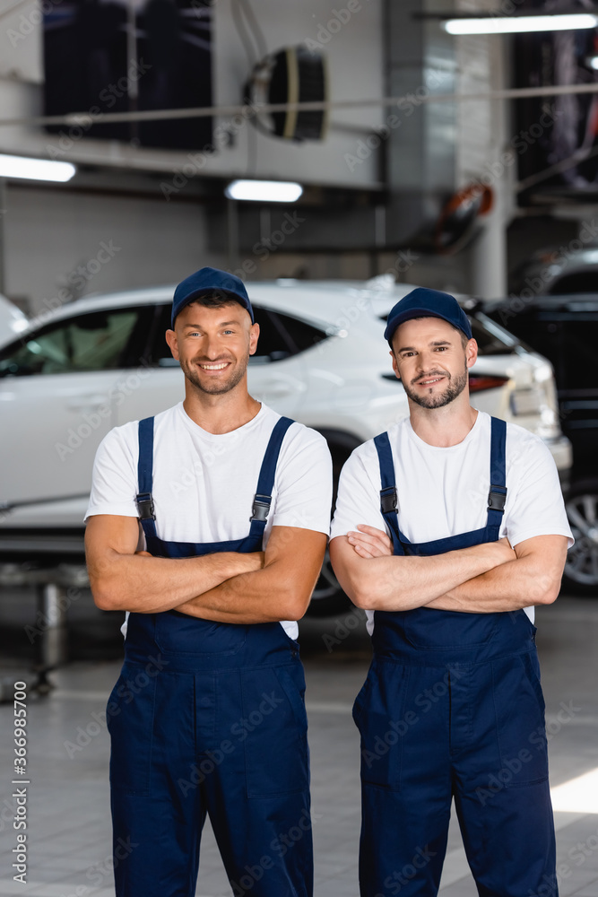 happy mechanics in uniform and caps standing with crossed arms in car service happy mechanics in uniform and caps standing with crossed arms in car service