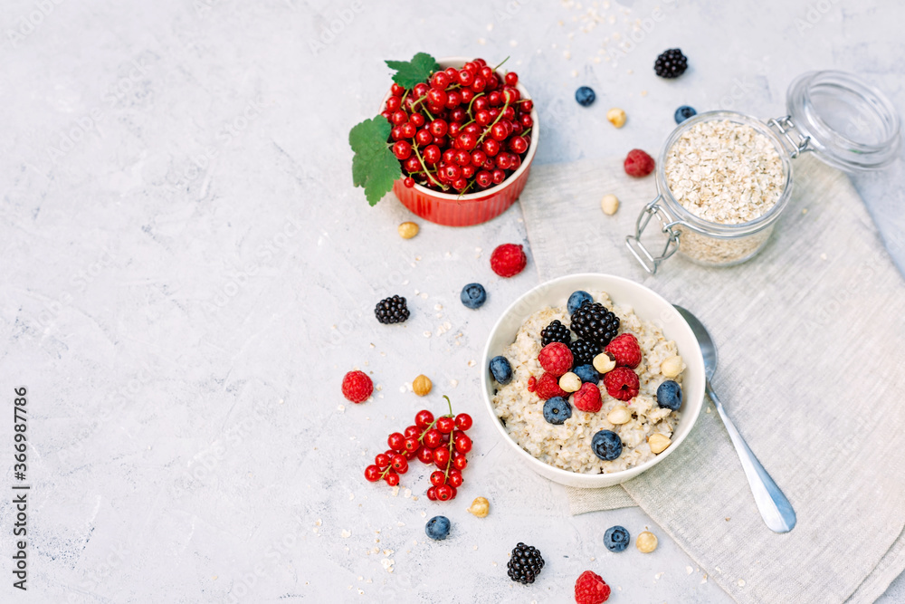 Oatmeal with raspberries, blueberries, blackberries, red currants and nuts on a gray concrete background. Healthy healthy breakfast. Oatmeal with raspberries, blueberries, blackberries, red currants and nuts on a gray concrete background. Healthy healthy breakfast.