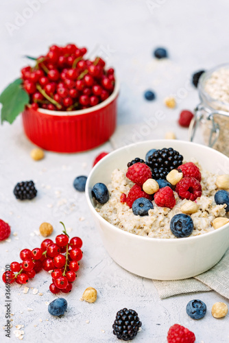 Oatmeal with raspberries  blueberries  blackberries  red currants and nuts on a gray concrete background. Healthy healthy breakfast.